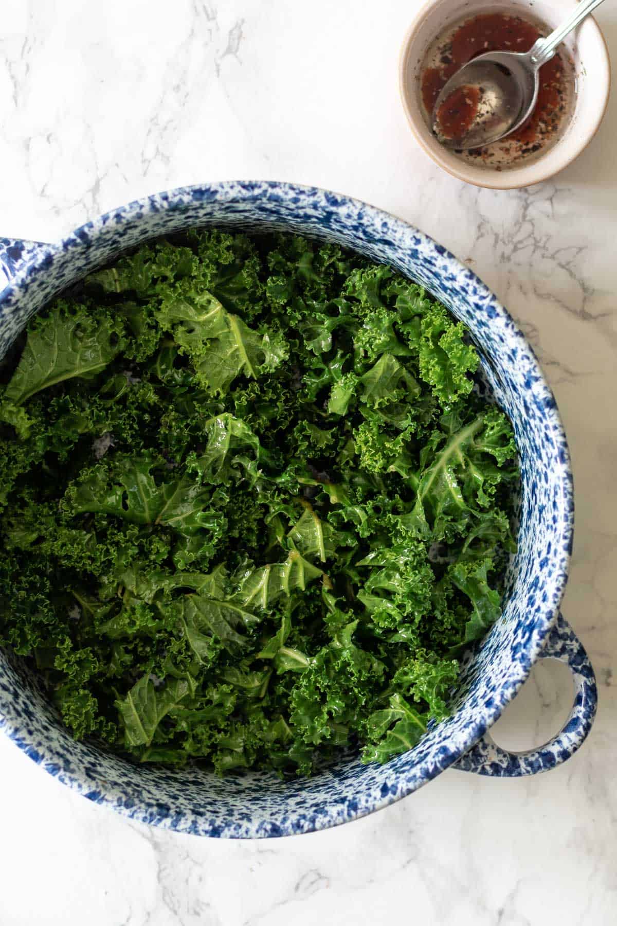 massaged kale in a bowl next to some salad dressing