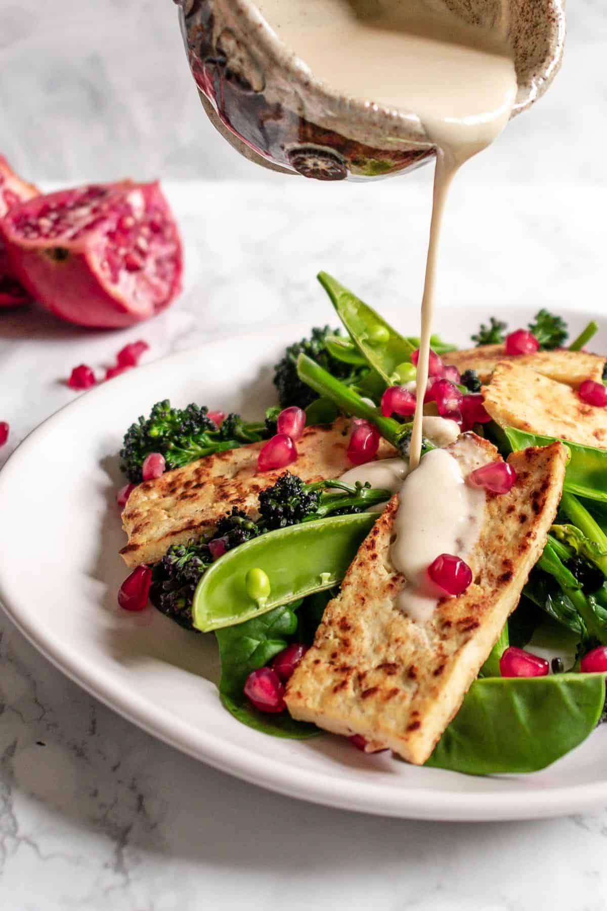 creamy tahini dressing being poured onto salad