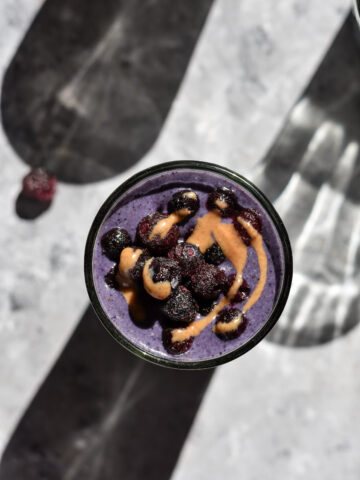 a glass of blueberry smoothie topped with almond butter