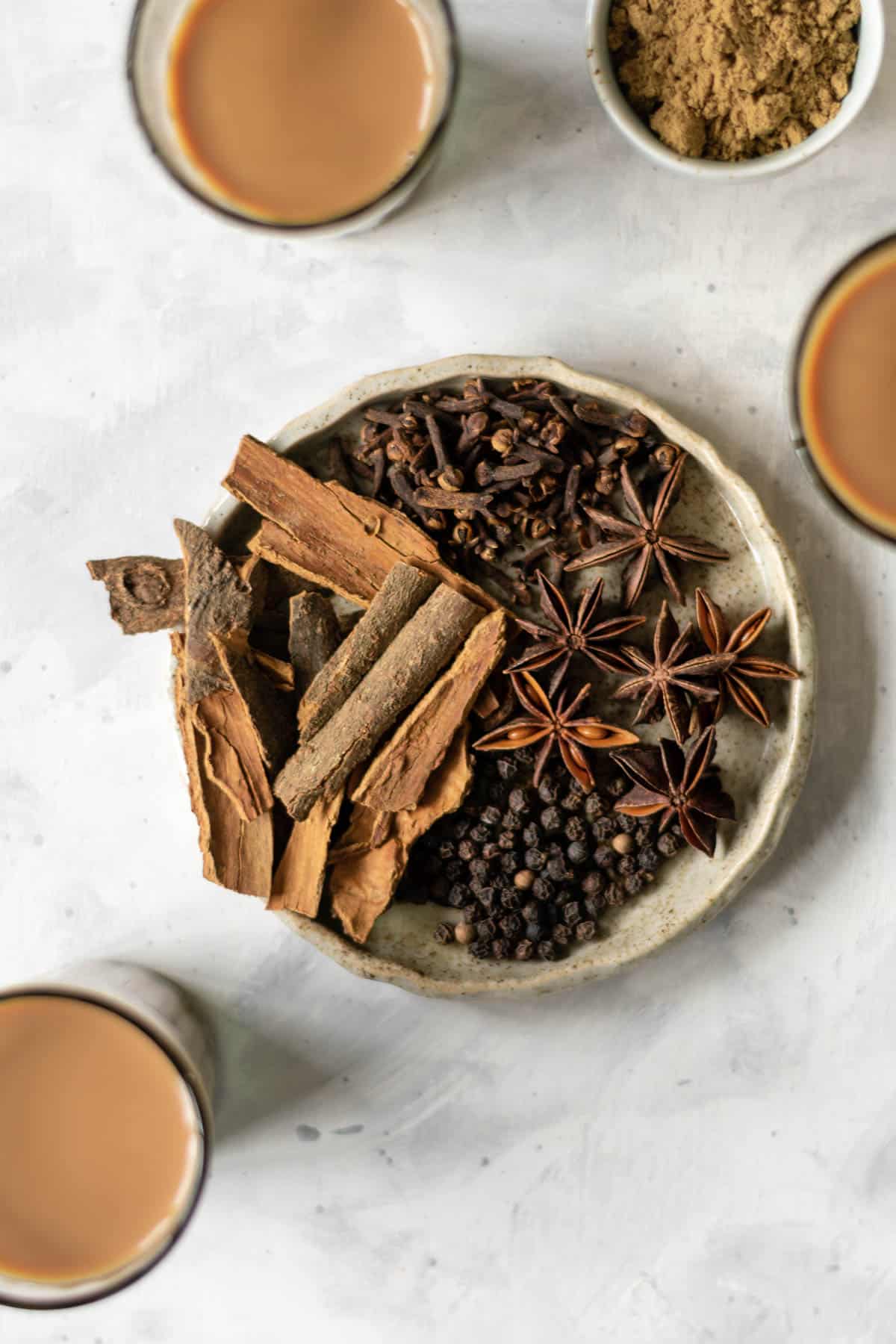 a plate of whole spices with chai mugs