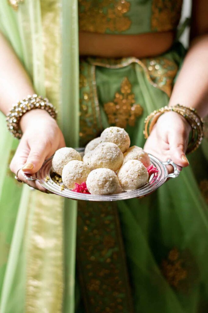a tray of coconut ladoos held by a girl in a lehenga