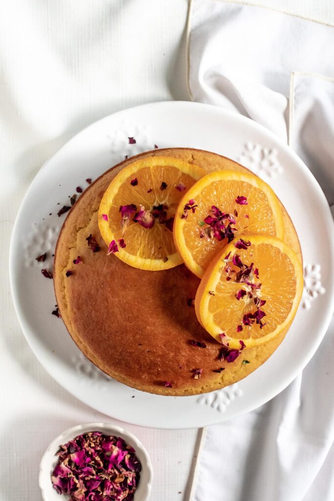 a polenta cake topped with orange slices and rose petals