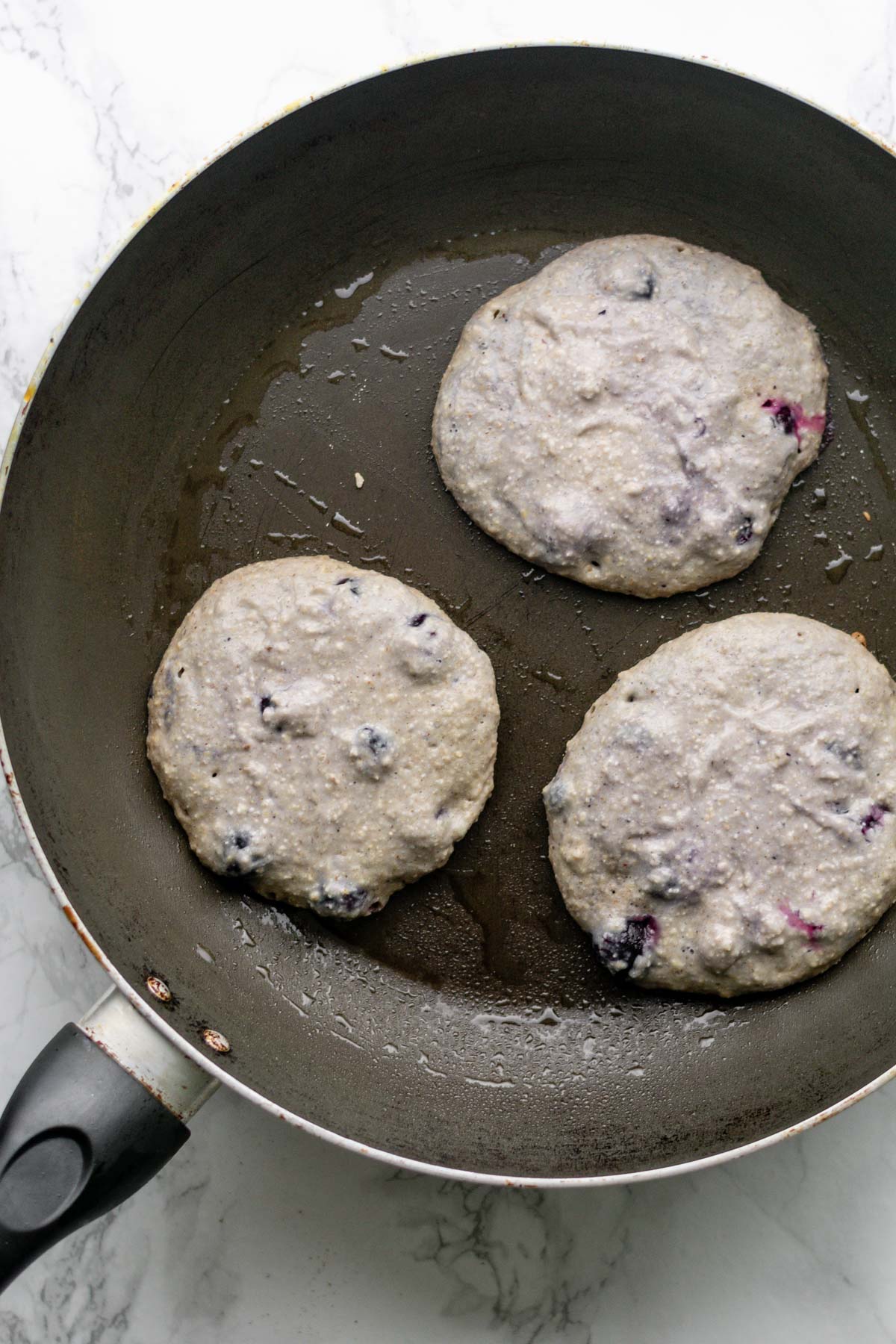 three blueberry pancakes being cooked in a pan