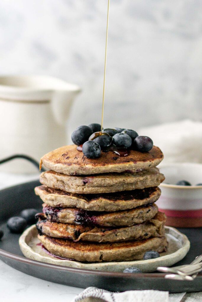 maple syrup being poured onto a stack of blueberry pancakes