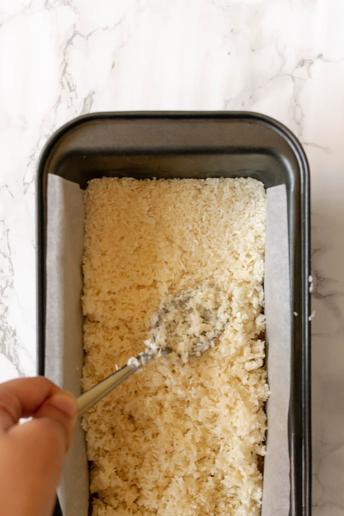 coconut filling being pressed into a loaf tin