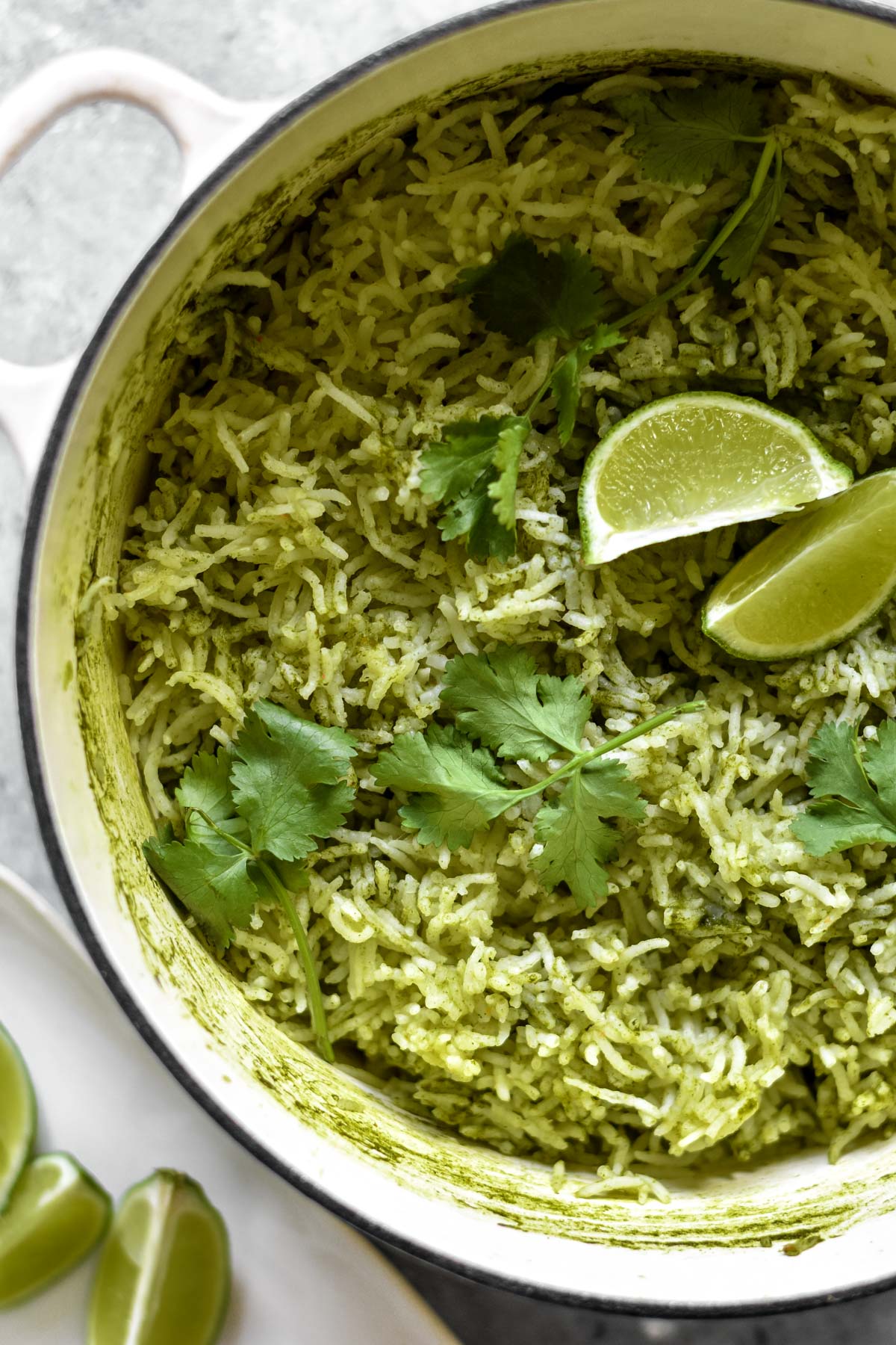 a pot of green rice topped with lime wedges and fresh coriander