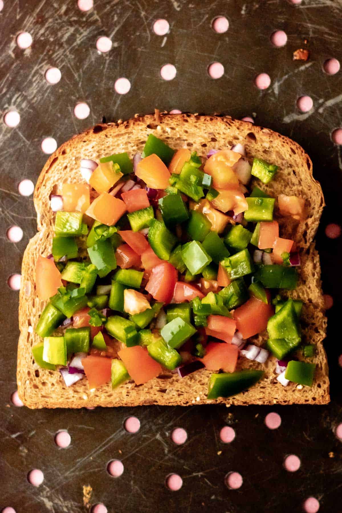 a slice of toast topped with chillies, tomato, pepper and red onion