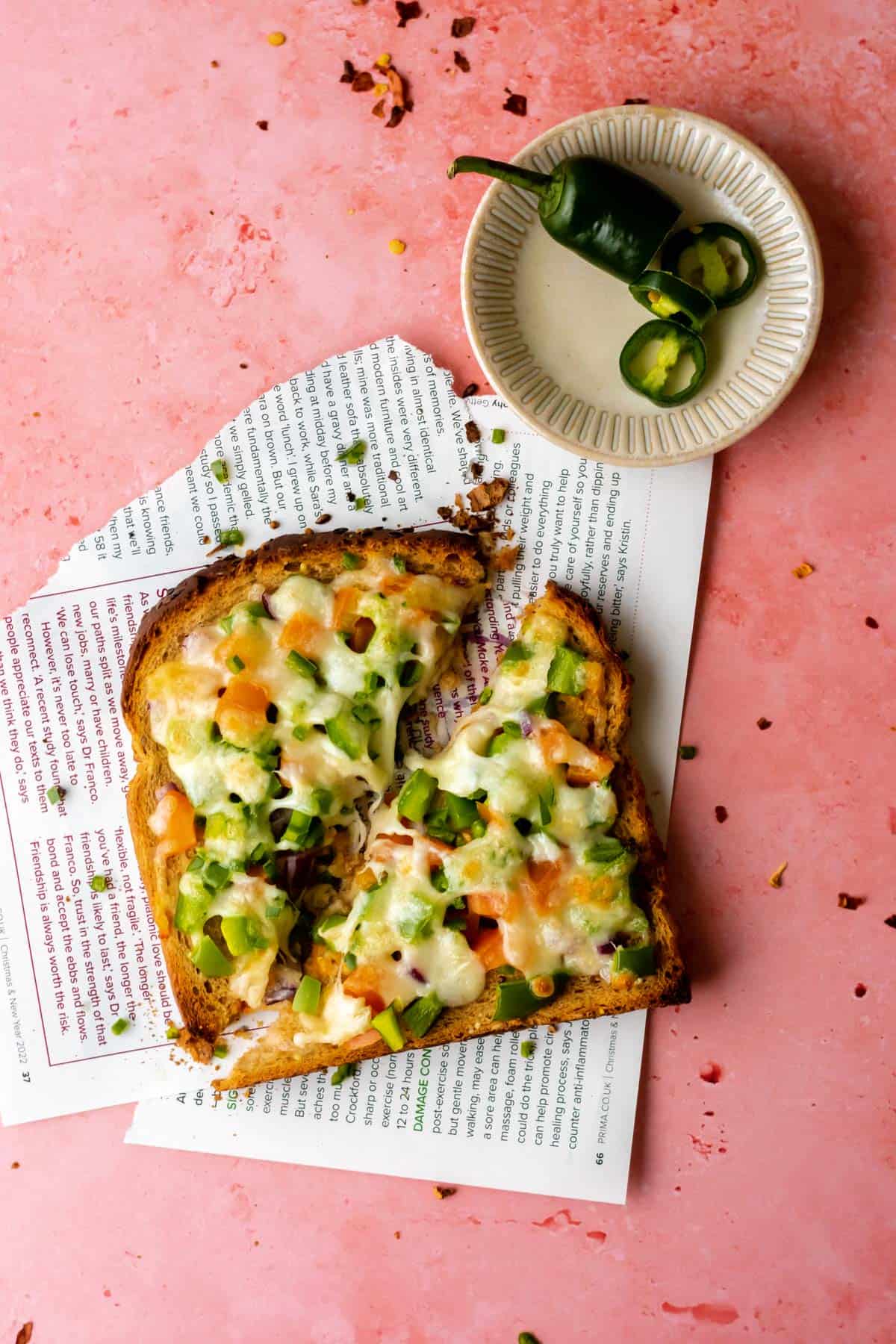 two triangles of chilli cheese toast next to a plate with green chillies on it