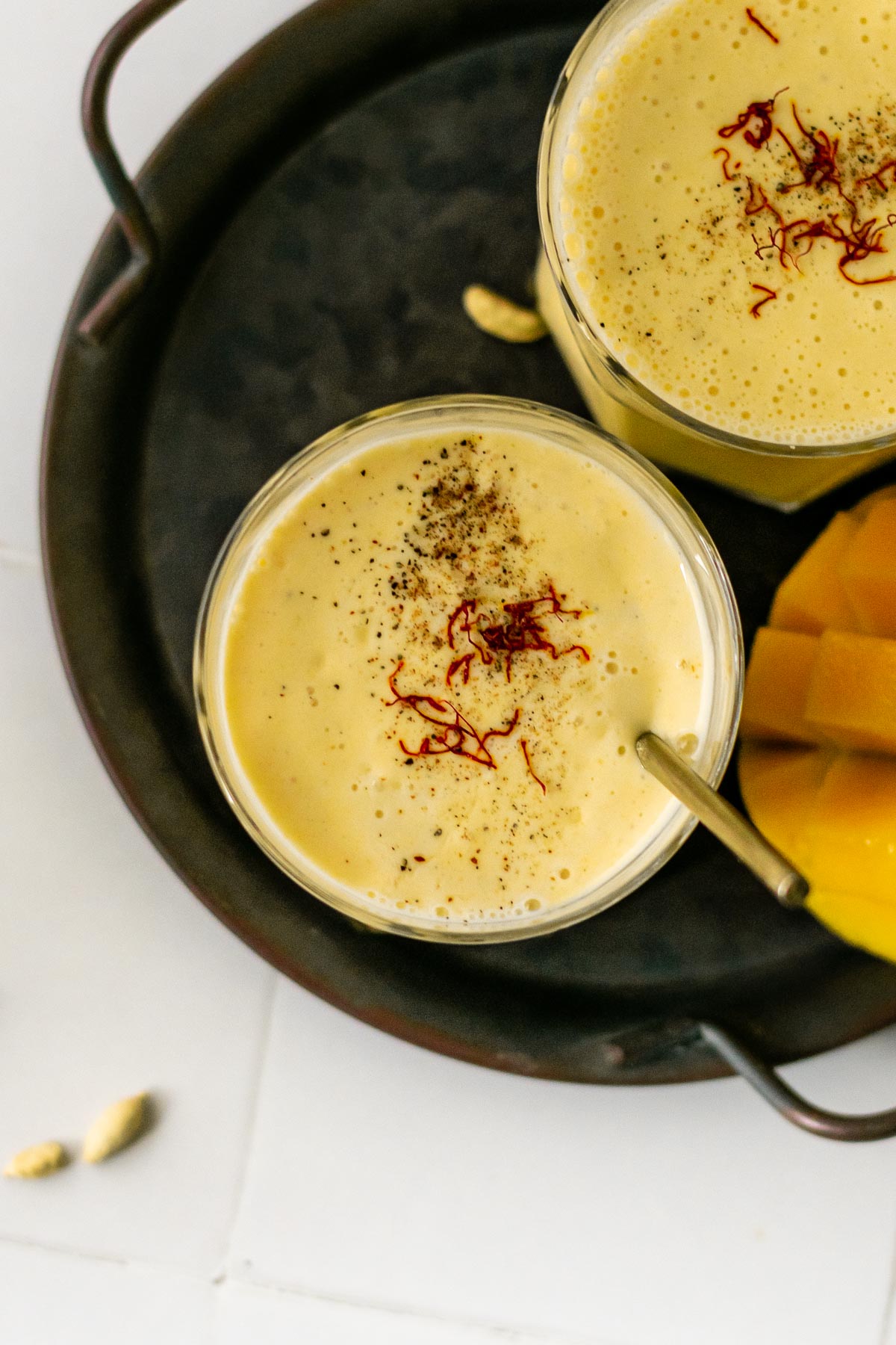 a glass of mango lassi topped with saffron and ground cardamom