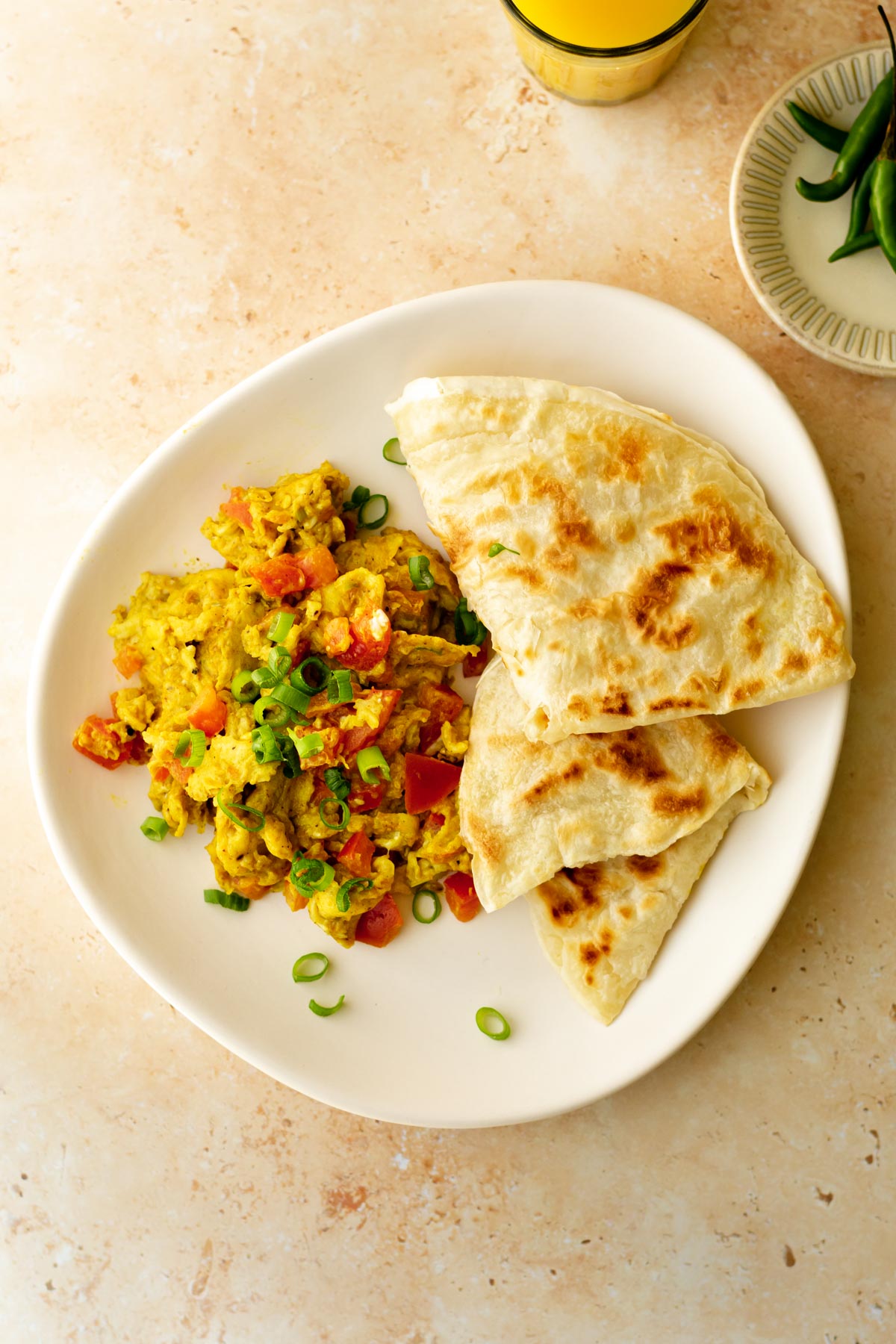 a plate of masala scrambled eggs topped with spring onion and served with paratha