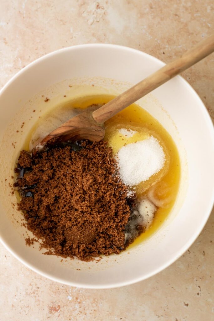 a mixing bowl containing browned butter, granulated sugar, and soft dark brown sugar.