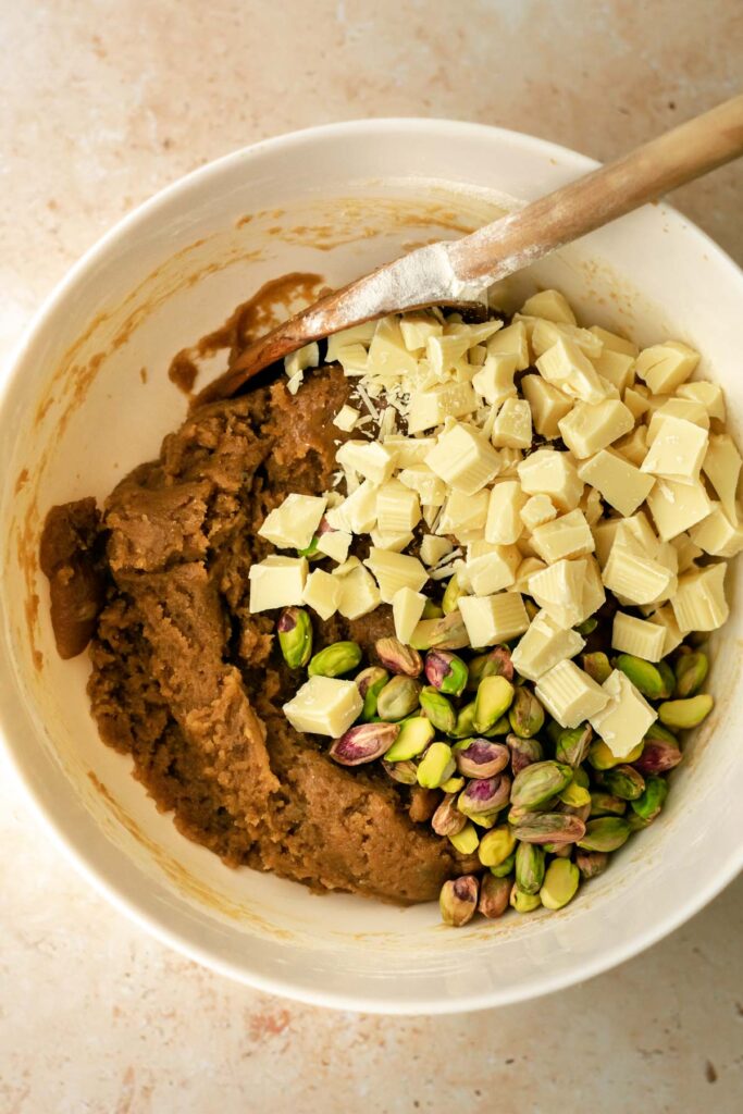 a bowl of cookie dough with whole pistachios and chunks of white chocolate.