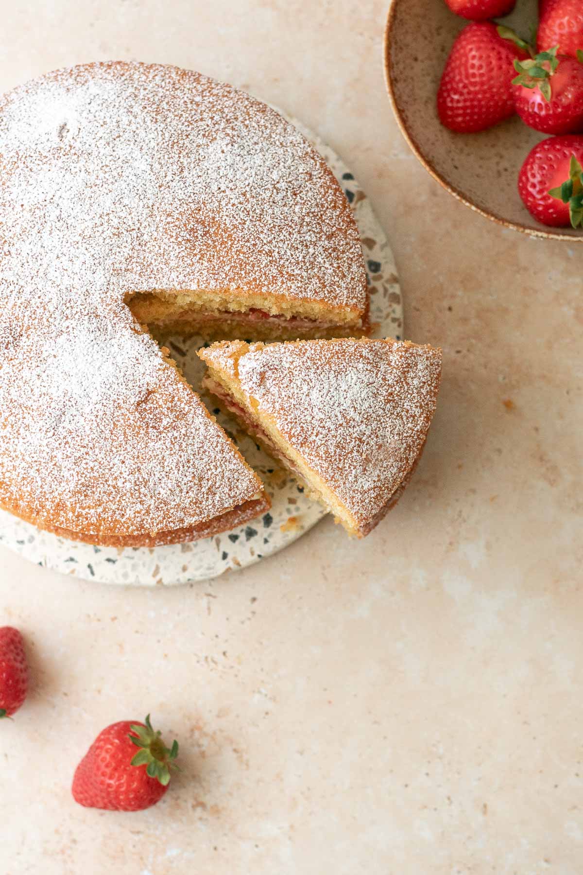 a victoria sponge cake pictured from above with a slice taken from it