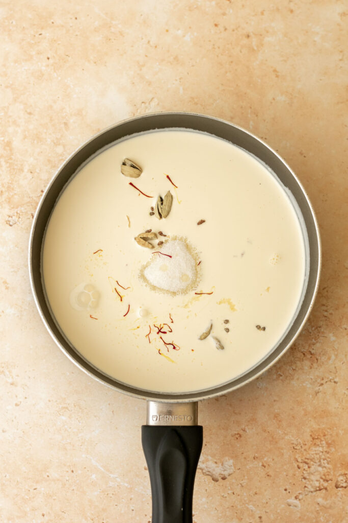 a saucepan containing heavy cream, cardamom pods, saffron, sugar and ginger.