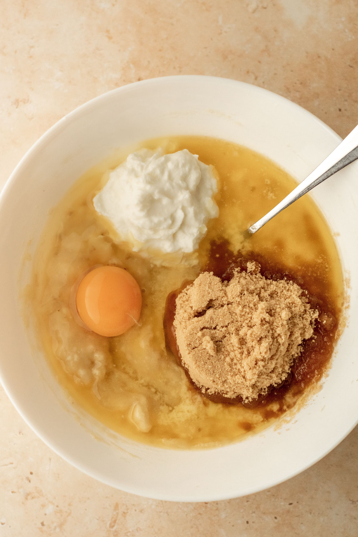 a bowl of mashed bananas with egg, sugar, yogurt and melted butter added