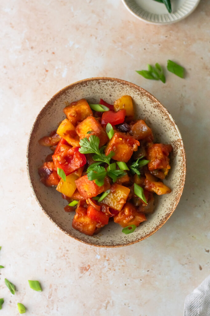 a bowl of chilli paneer garnished with onions and coriander