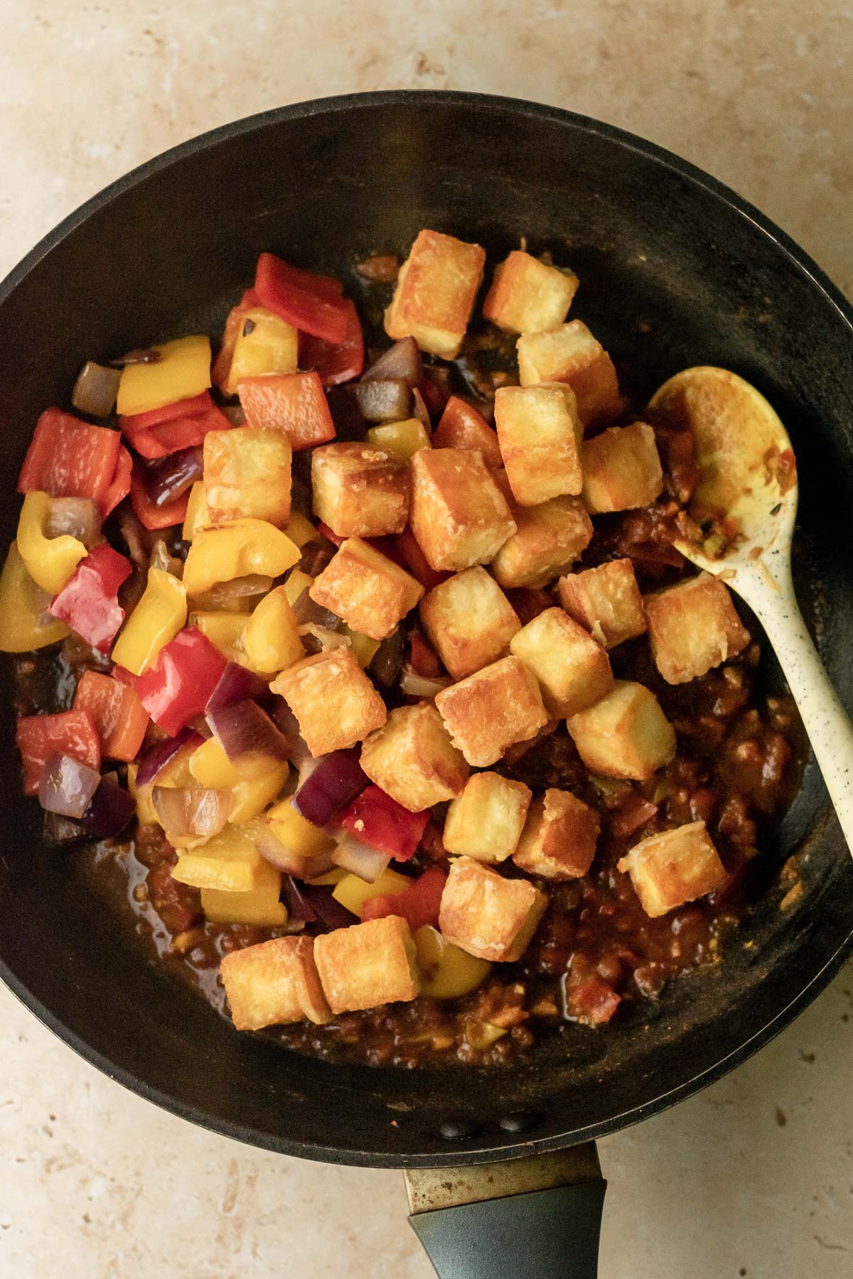 a frying pan with gravy, red peppers and onions, and cubes of crispy paneer