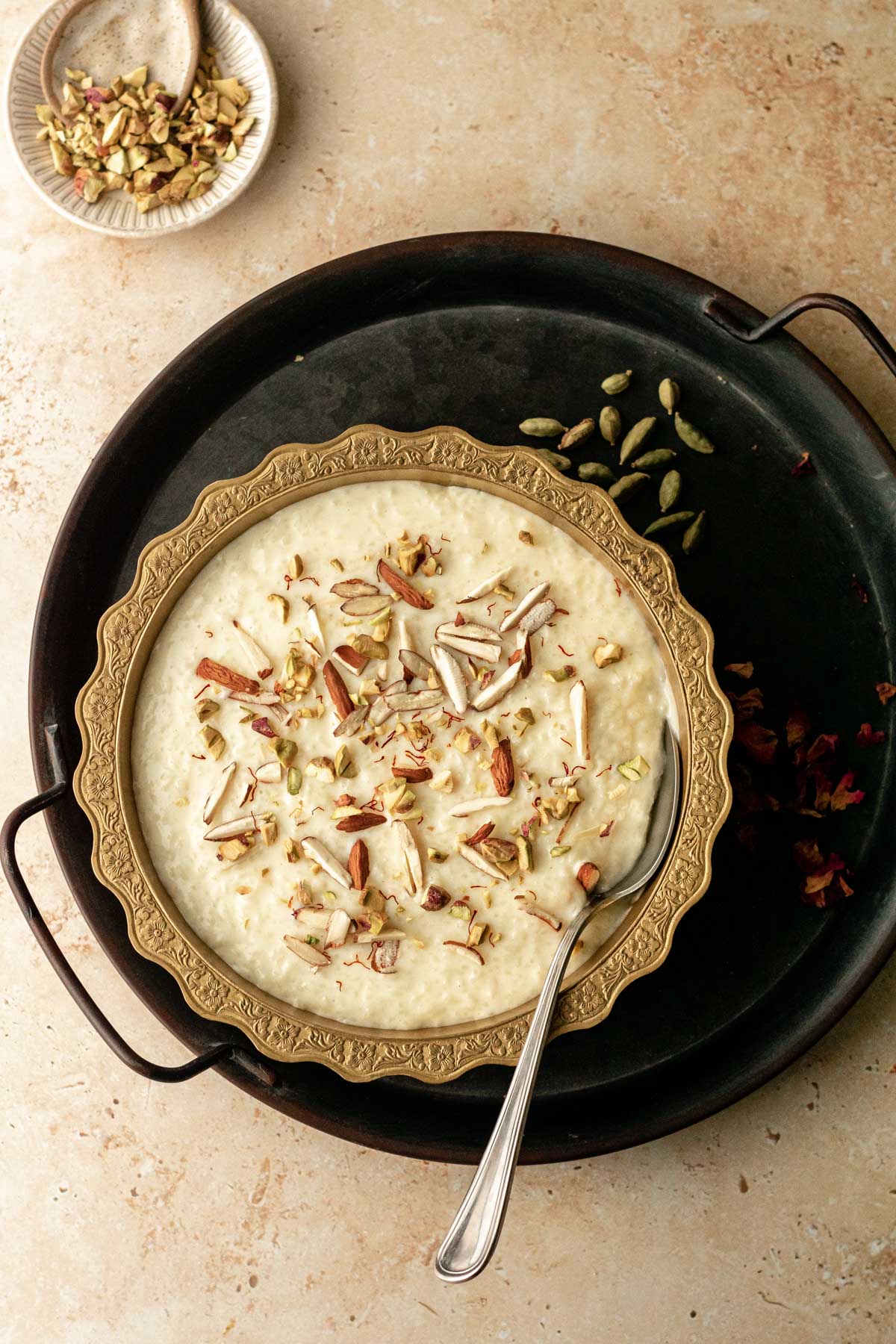 a bowl of kheer on a tray surrounded by garnishes