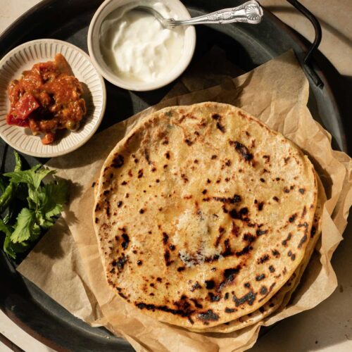 aloo parathas topped with ghee and served with chutneys and dahi