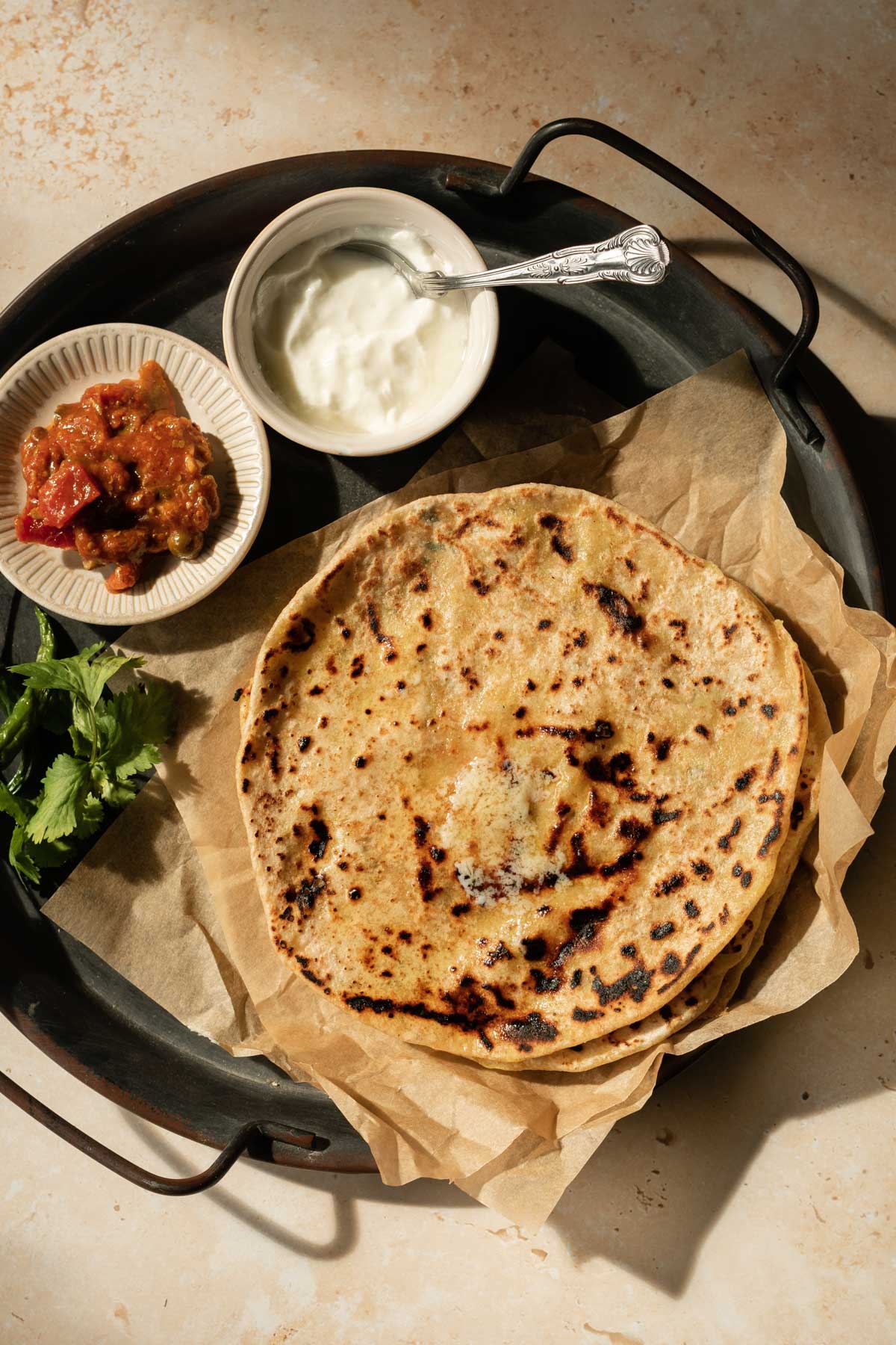 aloo parathas topped with ghee and served with chutneys and dahi
