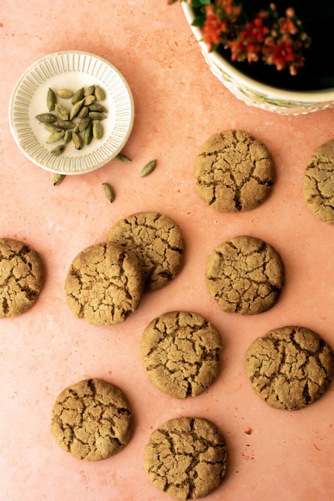 multiple cookies on a table with a bowl of cardamom pods