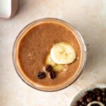 a glass of coffee flavoured smoothie topped with banana slices and coffee beans