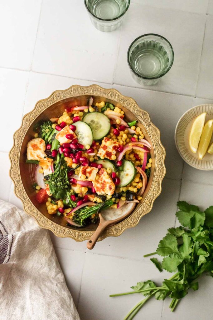 a bowl of salad next to some lemon wedges, herbs and glasses of water