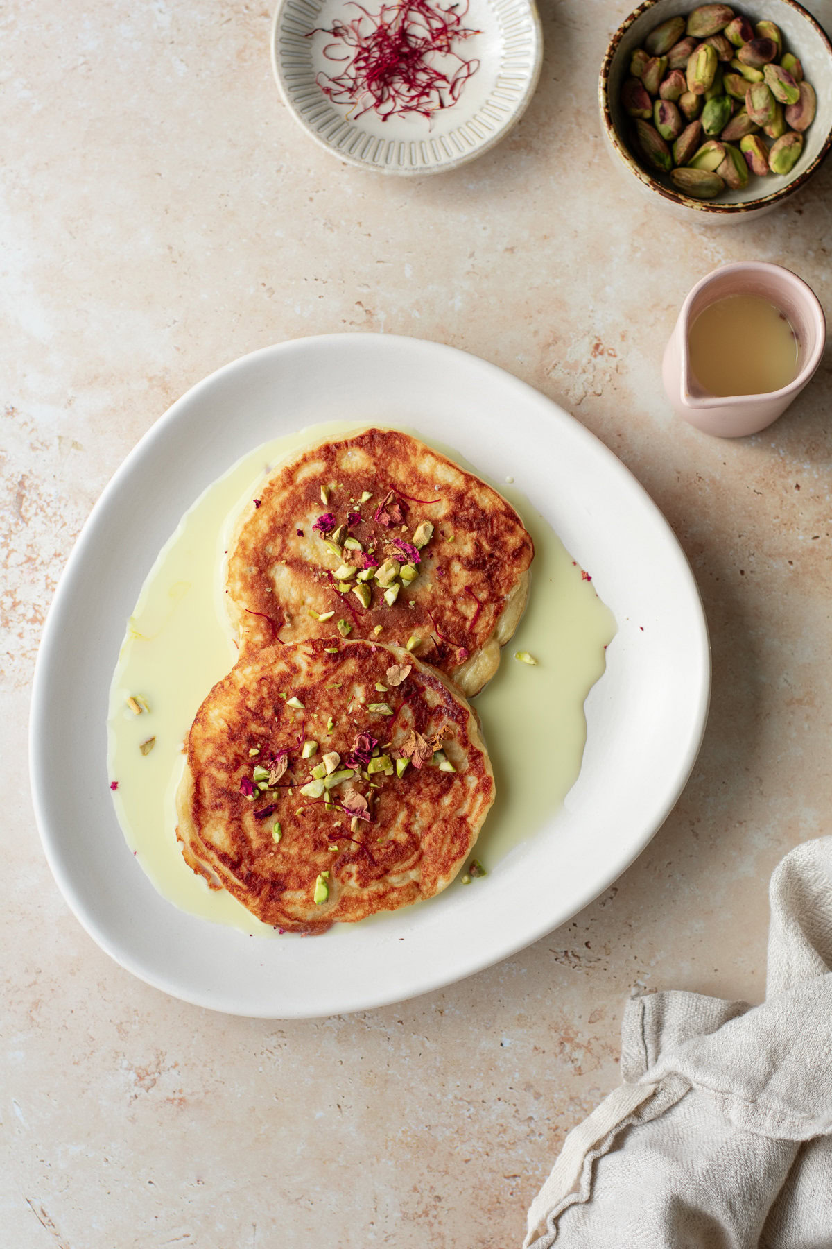 two pancakes on a plate in saffron milk, topped with pistachios