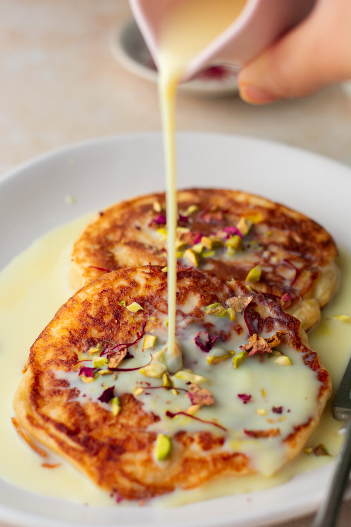 sweet saffron milk being poured onto rasmalai pancakes