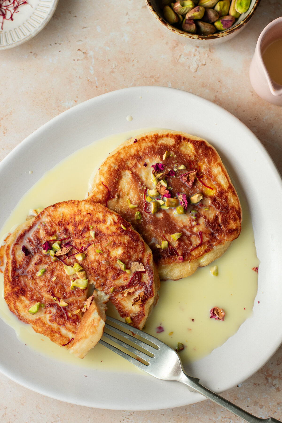 two rasmalai pancakes on a plate with a fork, served in sweet saffron milk