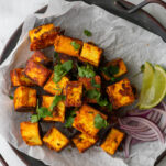 cubes of paneer tikka on a plate served with onion slices and lime wedges