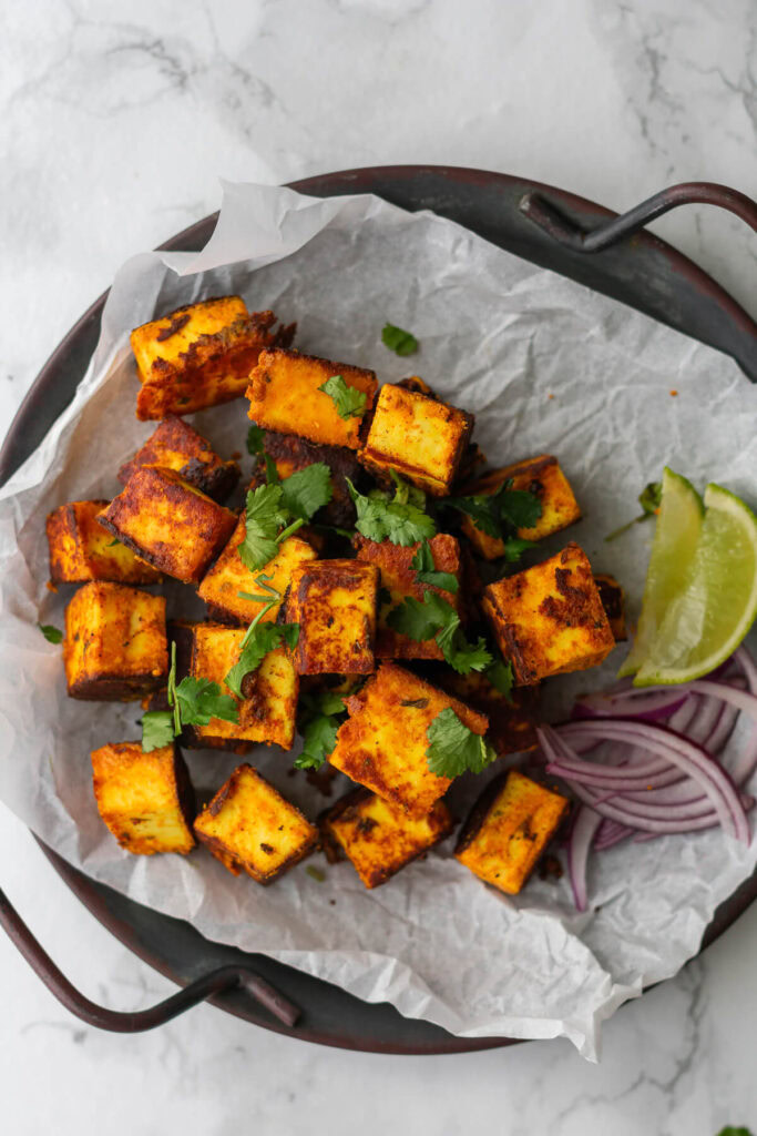 cubes of paneer tikka on a plate served with onion slices and lime wedges