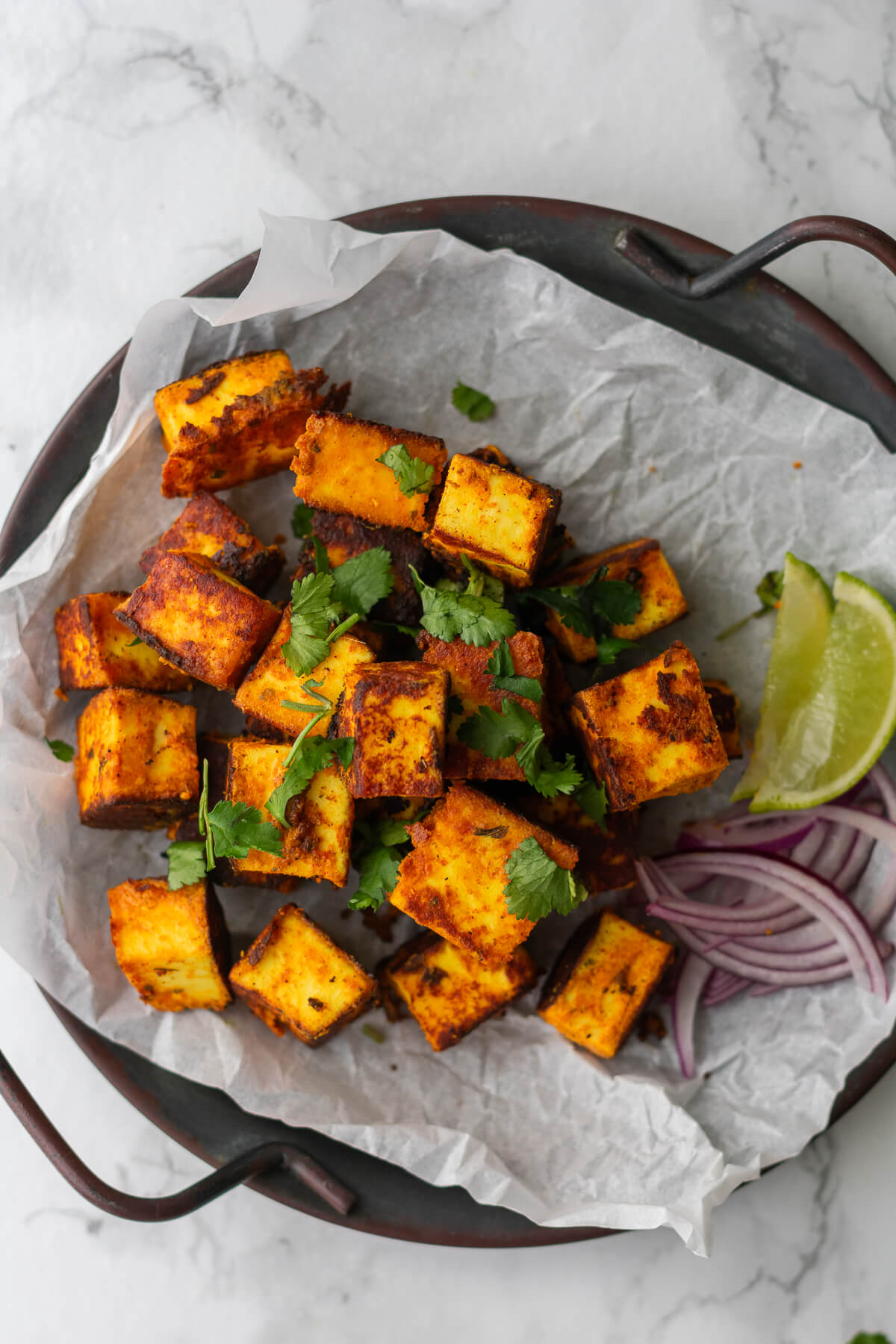 cubes of paneer tikka on a plate served with onion slices and lime wedges
