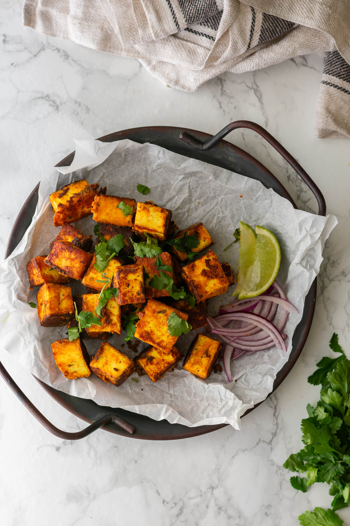a plate of paneer tikka served with coriander, lime wedges and red onion slices