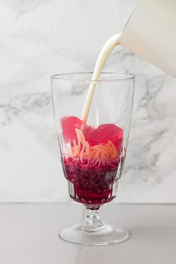 milk being poured into a glass of rose syrup, basil seeds, vermicelli and rose jelly